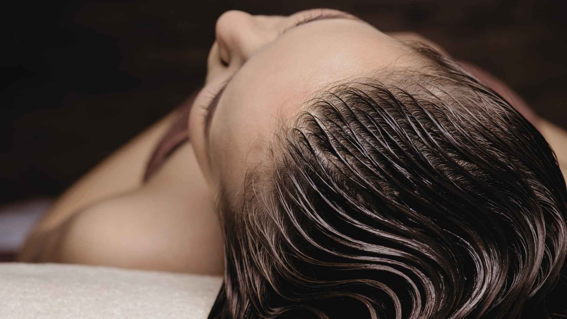 Gros plan d'une femme avec des cheveux humides soigneusement peignés en arrière, illustrant un moment de soin capillaire haut de gamme.