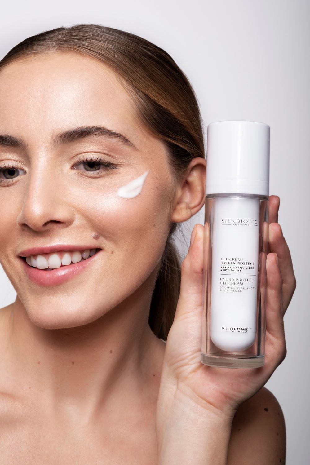 Modèle souriante tenant un soin visage Silkbiotic, hydratation et éclat naturel.